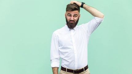 A bearded man scratching his head