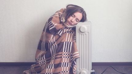 Cold woman wrapped in blanket next to radiator