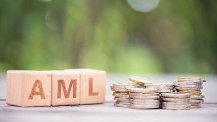 AML written on wooden blocks next to a piles of coins