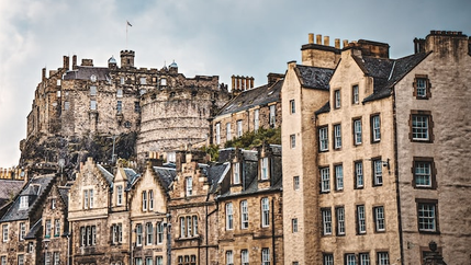 Edinburgh Castle above rooftops of old stone townhouses on a cloudy day