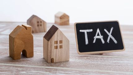 Tax written on chalkboard next to some model houses